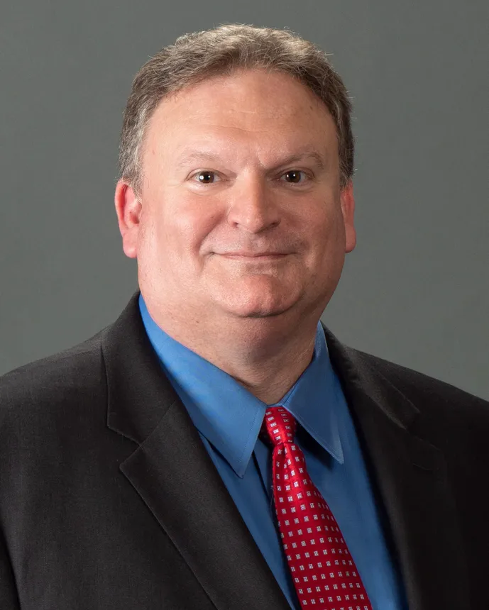 Man in a dark suit with a blue shirt and red tie.