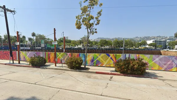 A city street with a colorful mural-lined fence blocking off a large property.