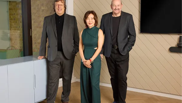 Three executives from consultant R3 stand on a wood floor in formal attire