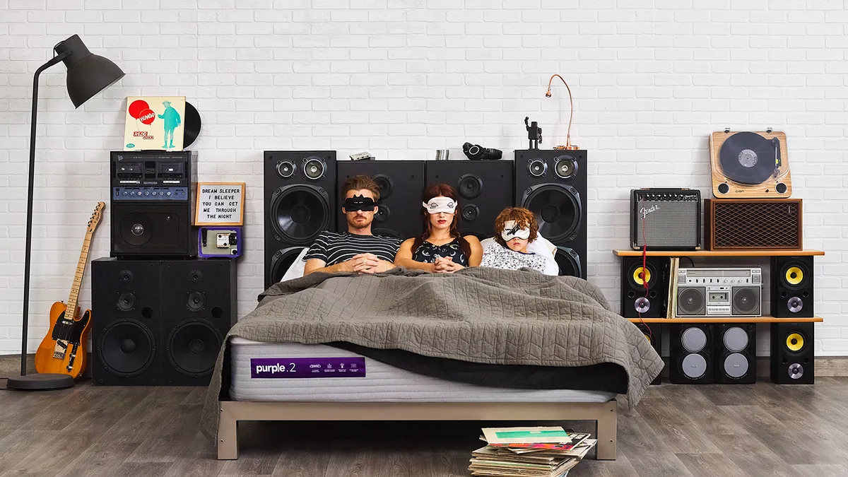 Three people in bed with eye masks on surrounded by audio equipment.