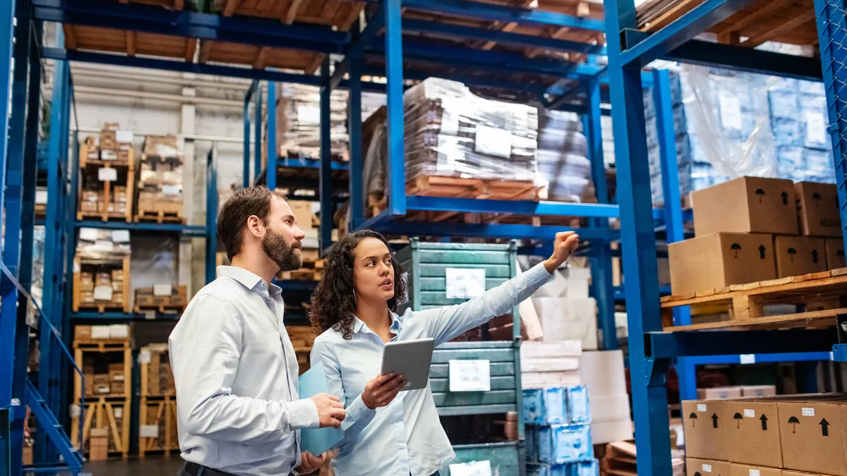 Businesswoman with a digital tablet showing and talking with male worker in distribution warehouse. Manager working with foreman in warehouse checking stock levels.