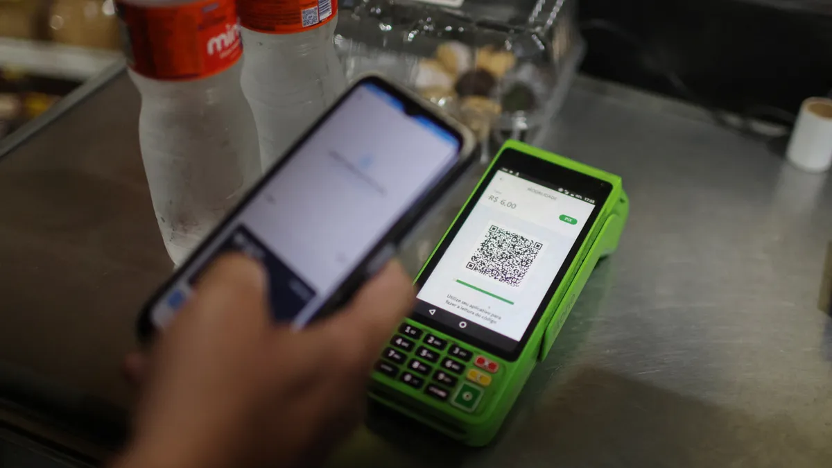 A hand holding a phone hovers the phone over a point-of-sale reader on a sitting on a countertop.