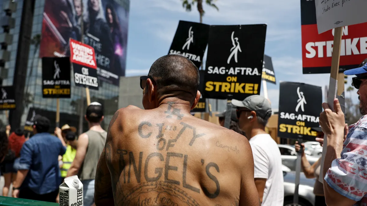 A man's shirtless back has a tattoo that reads "City of Angels."