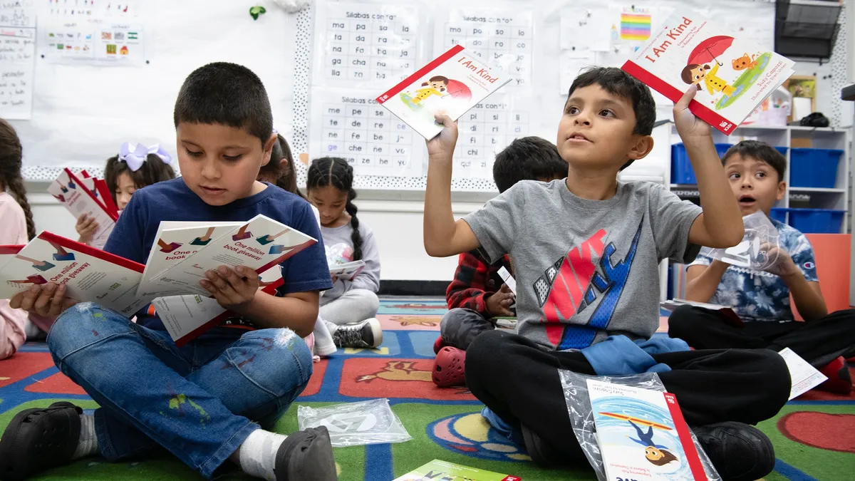 Students sit on the floor of a classroom holding books