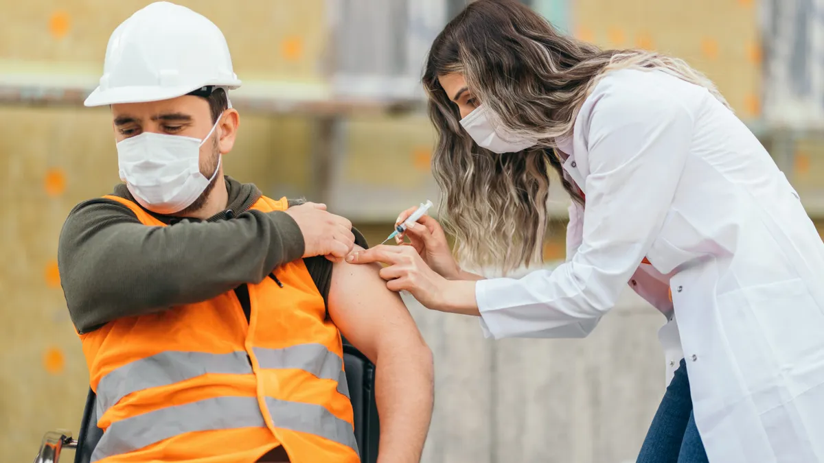 A nurse inoculates a construction worker against COVID-19.