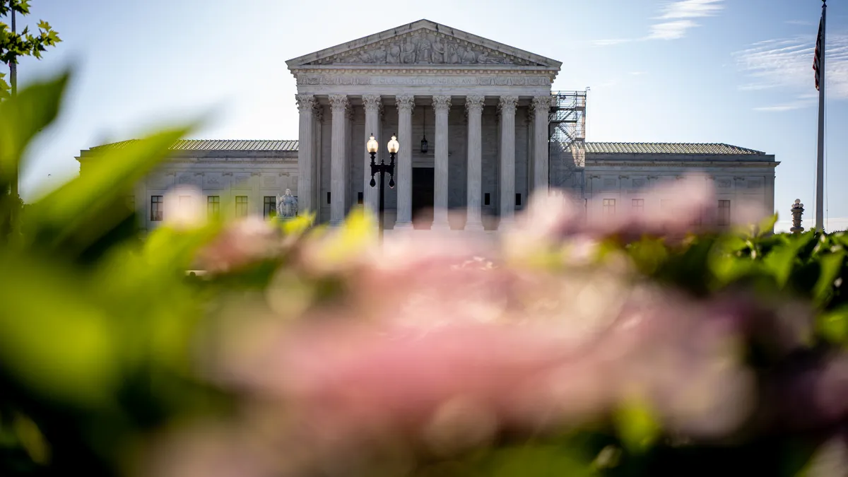 The U.S. Supreme Court building's facade with flowers blurred in the foreground.