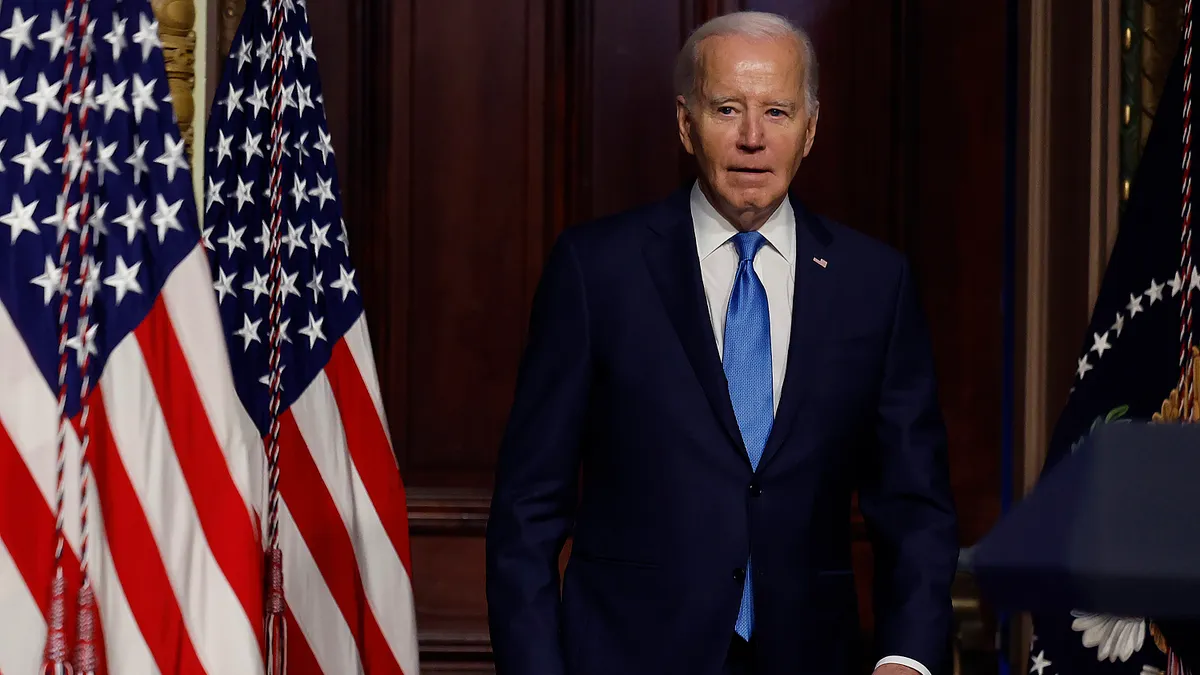 A man in a suit stands in front of several flags.