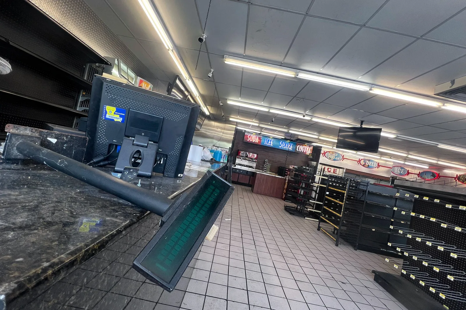 The inside of a convenience store with a broken cash register and empty shelves.