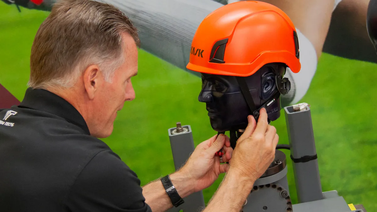 A man straps a safety helmet onto a dummy's head.