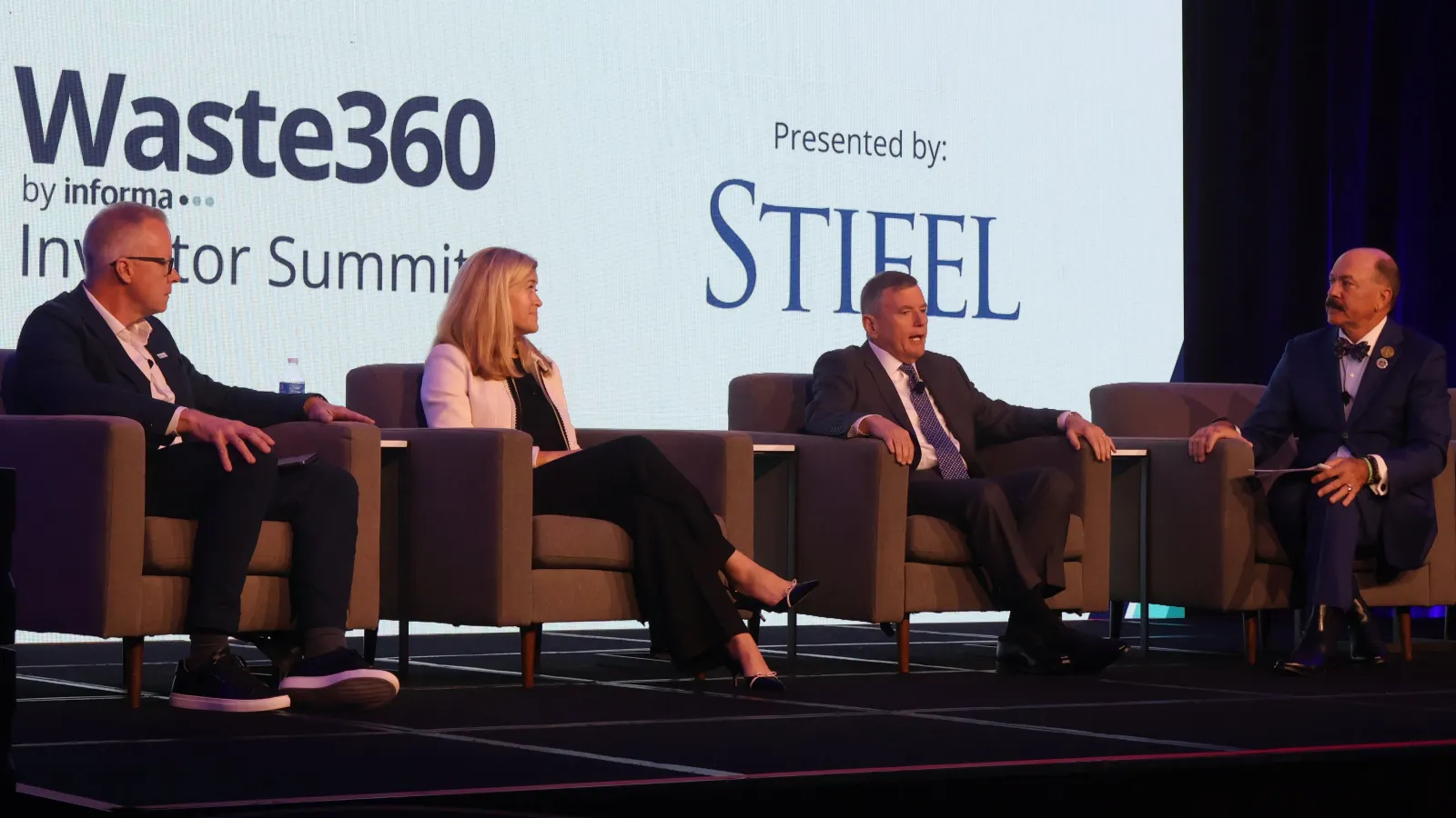 Three people sit on stage with a large screen behind them that reads: "Waste360 by Informa: Investor Summit. Presented by: Stifel."