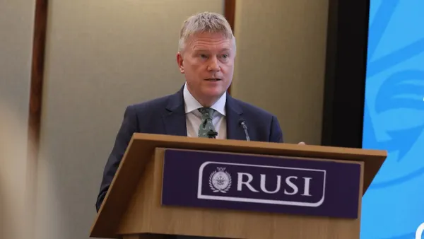 A man stands at a lectern that has a plaque bearing the acronym "RUSI"