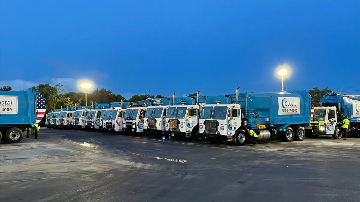 Row of waste collection trucks in parking lot