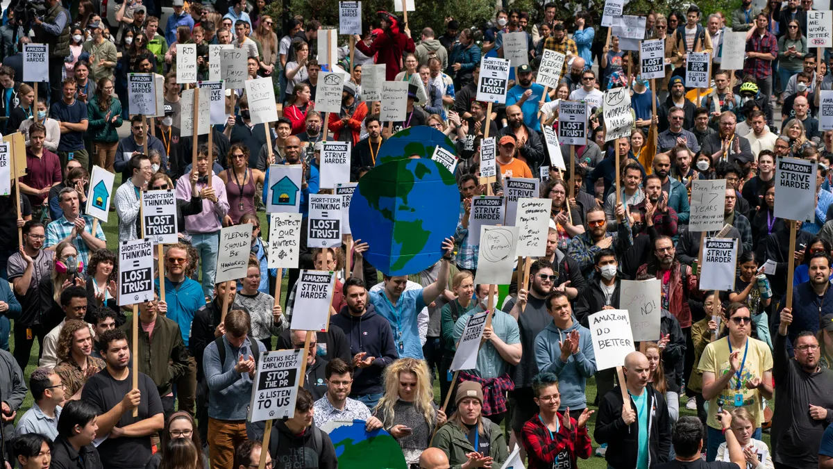 A group of approximately 100 protesters holding climate change protest signs stand outside, with a large cardboard globe in the middle of the group.