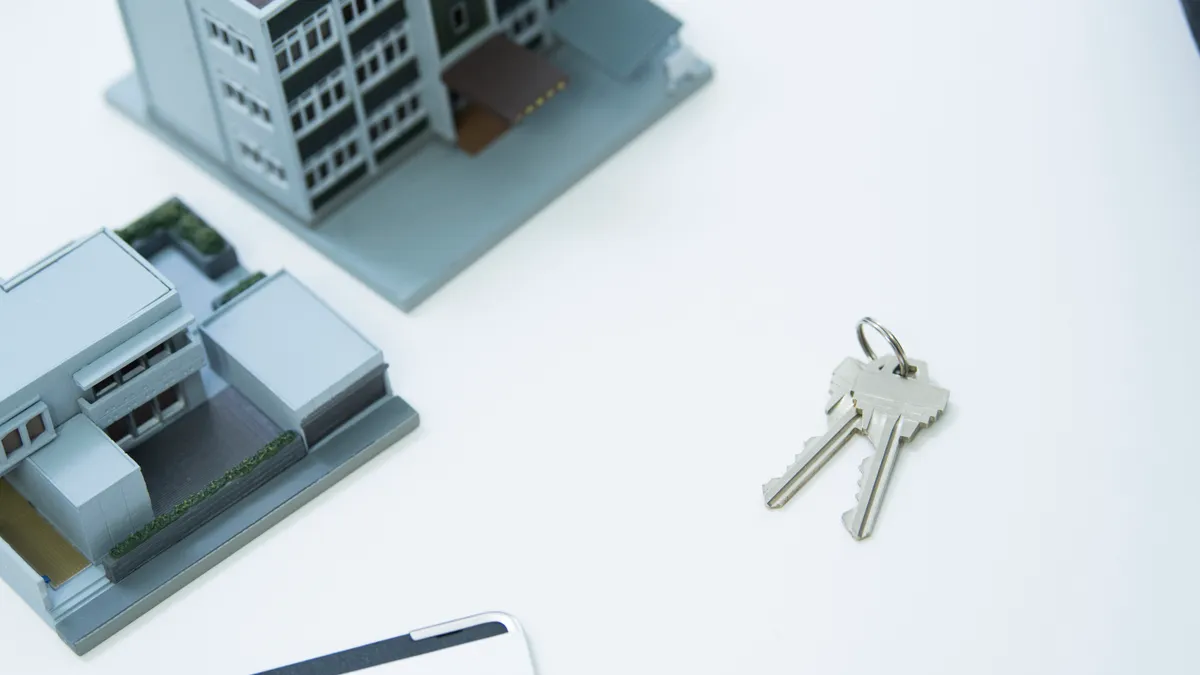 Two models of the building, two keys of the house and a binder on the white table.