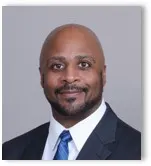 A close-up of a person wearing a suit and tie and smiling for a photo
