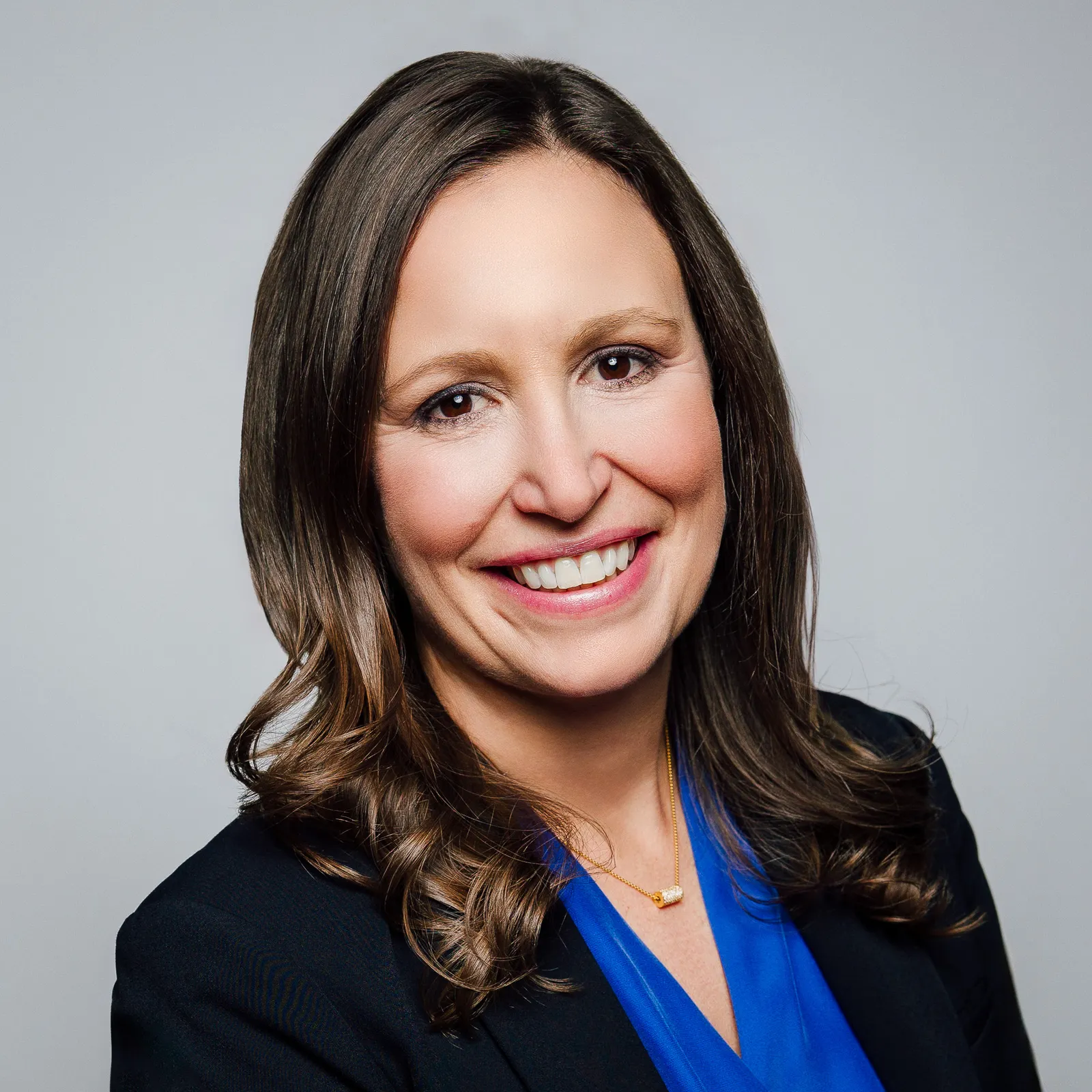 A person wearing a dark blazer and blue blouse smiles for the camera.