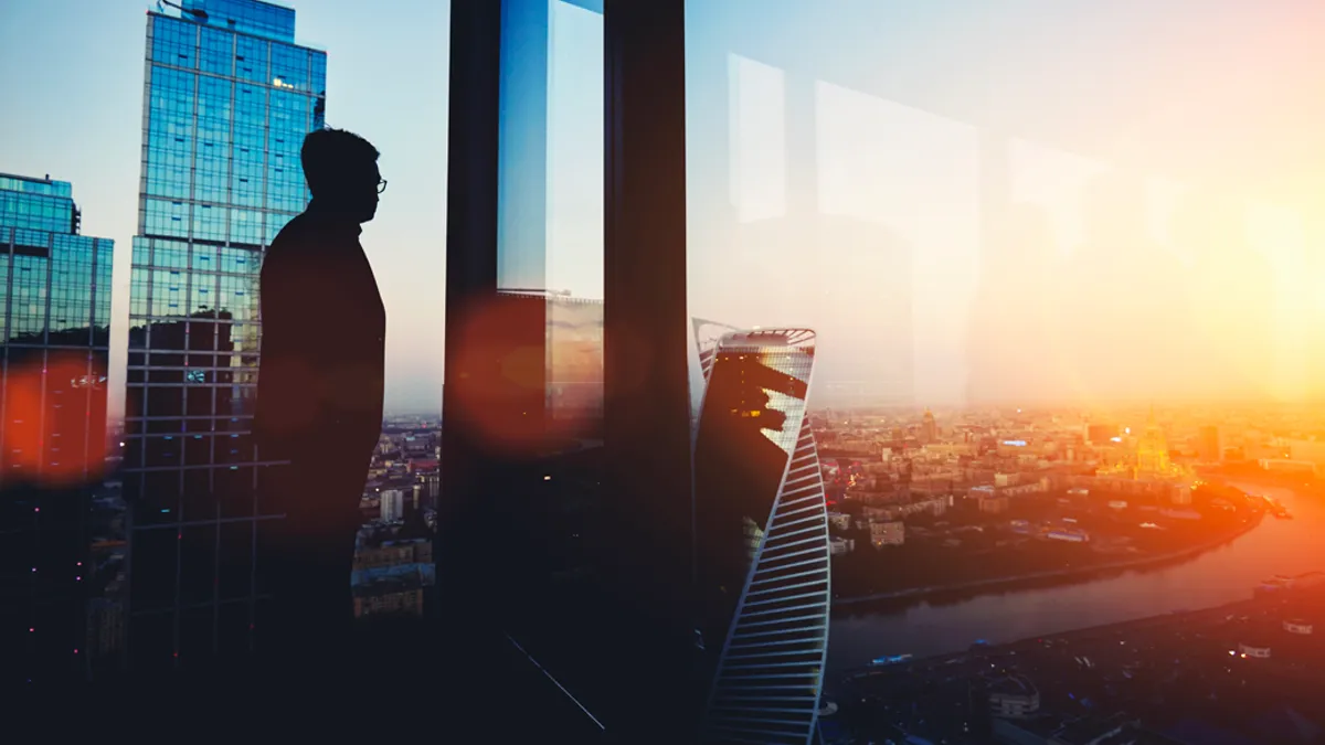 Silhouette of a man staring out at the view of a city from the window of a tall building