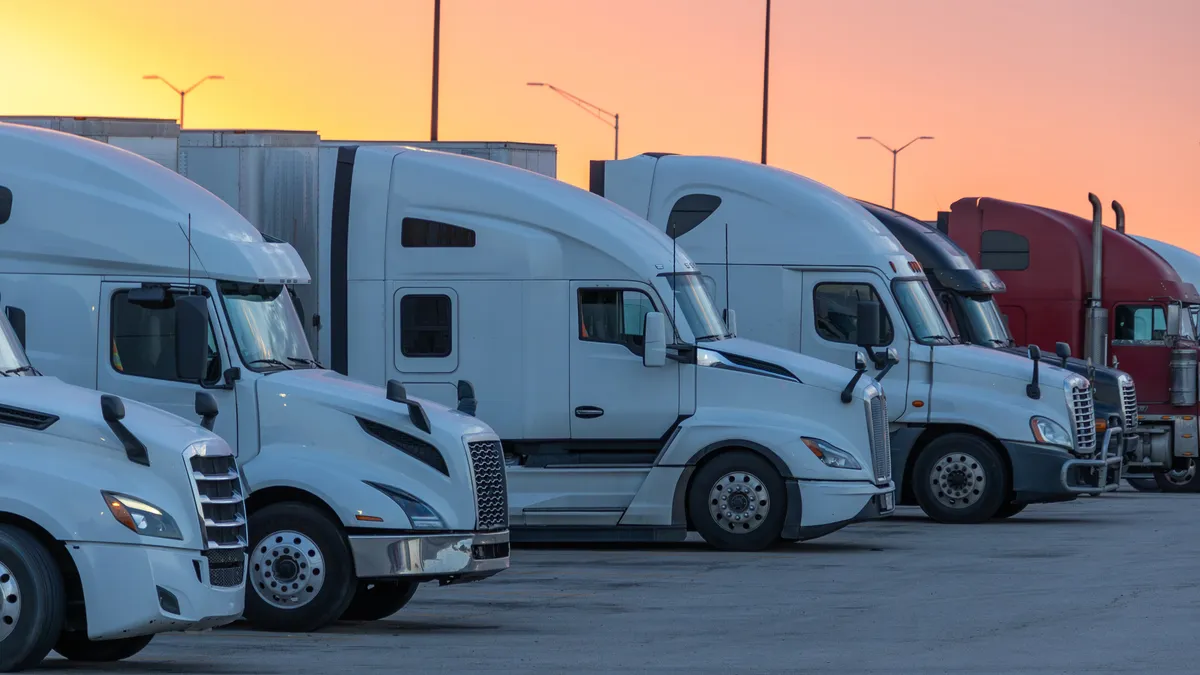 Rows of trucks parked at a rest stop against a yellow and pink sunset.