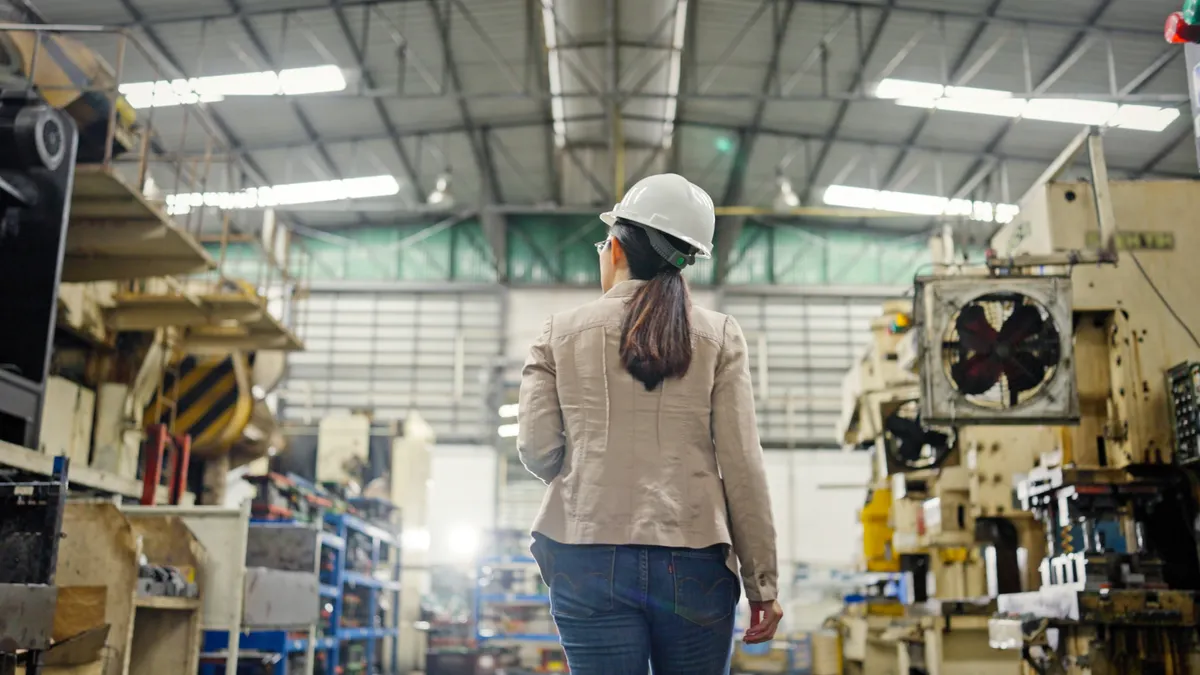 A factory worker stands with their back to the camera in a factory setting.