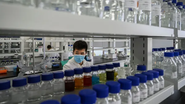 A technician wearing a blue mask works in a laboratory.