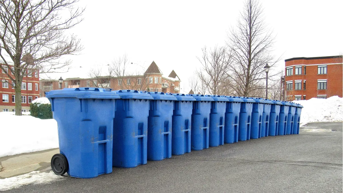 A row of blue recycling carts on a street in Canada, snow in background