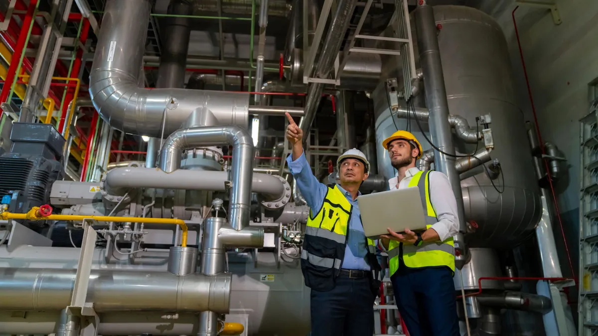 Two male electrical engineers in safety uniform work together at a factory site control room.