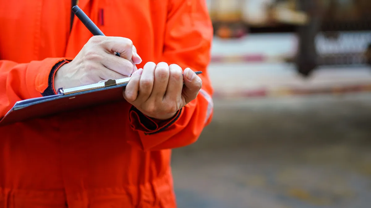 A close-up image of a person in brightly colored safety gear writing on a clipboard.