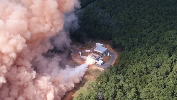 A large cloud of peach-shade smoke emitted from a rocket in a rural area.