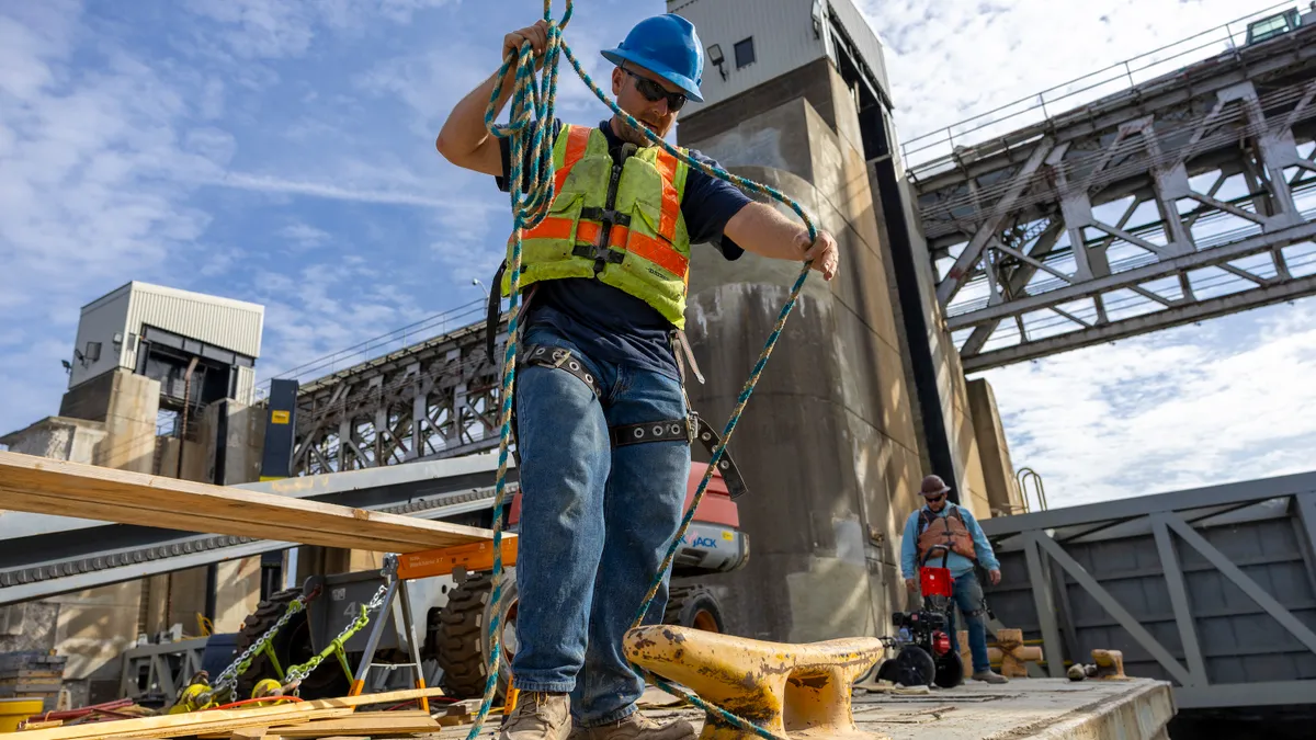 A man in safety gear moves with a rope on a metal structure.