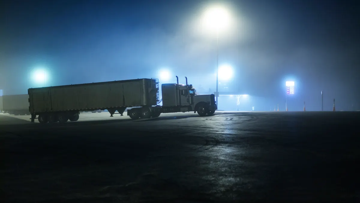 Bright street lights way up high slice through dense fog to illuminate a dark interstate expressway rest stop parking lot at midnight