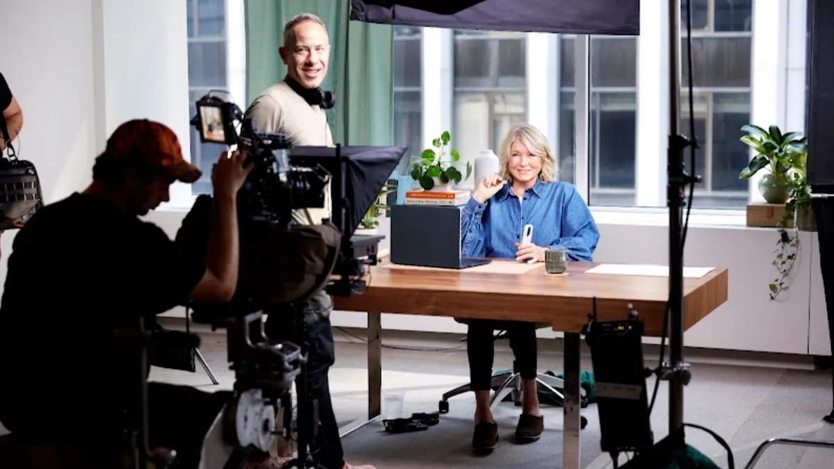 Martha Stewart sits behind a desk surrounded by a film crew.