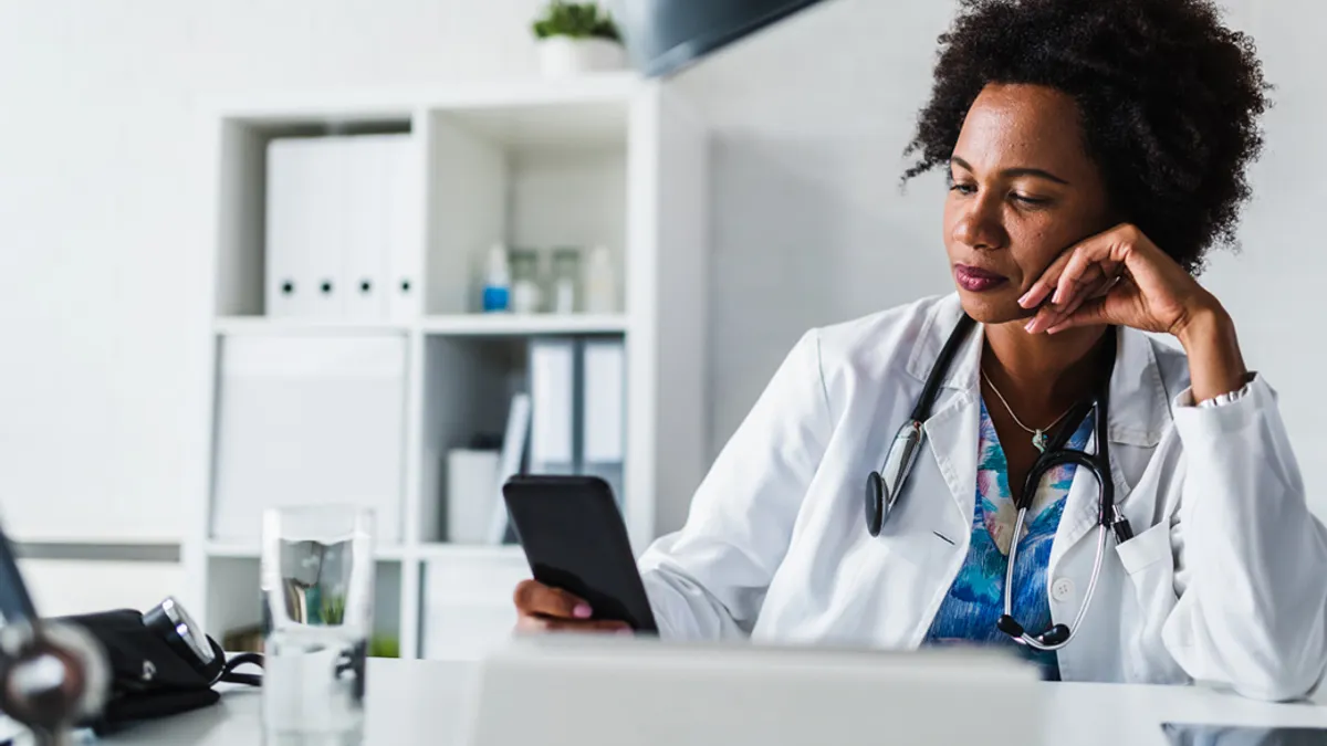 Doctor sits at her office and using mobile smart phone