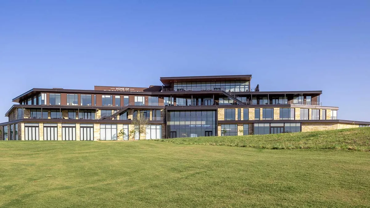 Four-story glass and sandstone building with a vast green lawn in front of it.