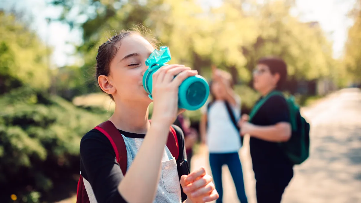 Schoolgirl wearing red backpack drinking water at schoolyard on a sunny day