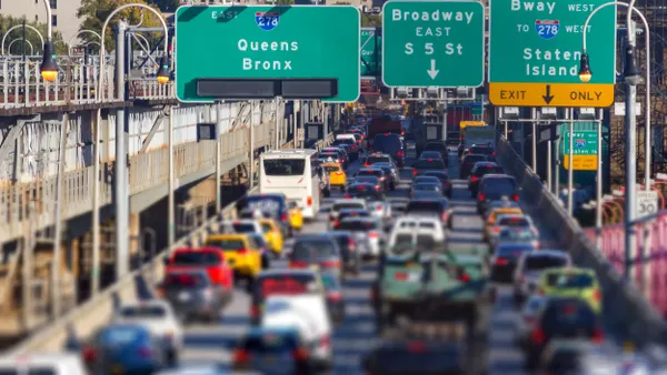 A street on a bridge filled with cars, green signs say "Queens Bronx," "Broadway East S 5 St," "Bway West to 278 West Staten Island Exit Only."