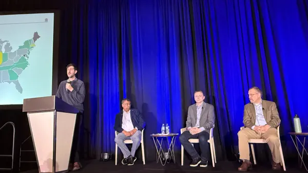 Men sit on a stage and a man speaks at a podium