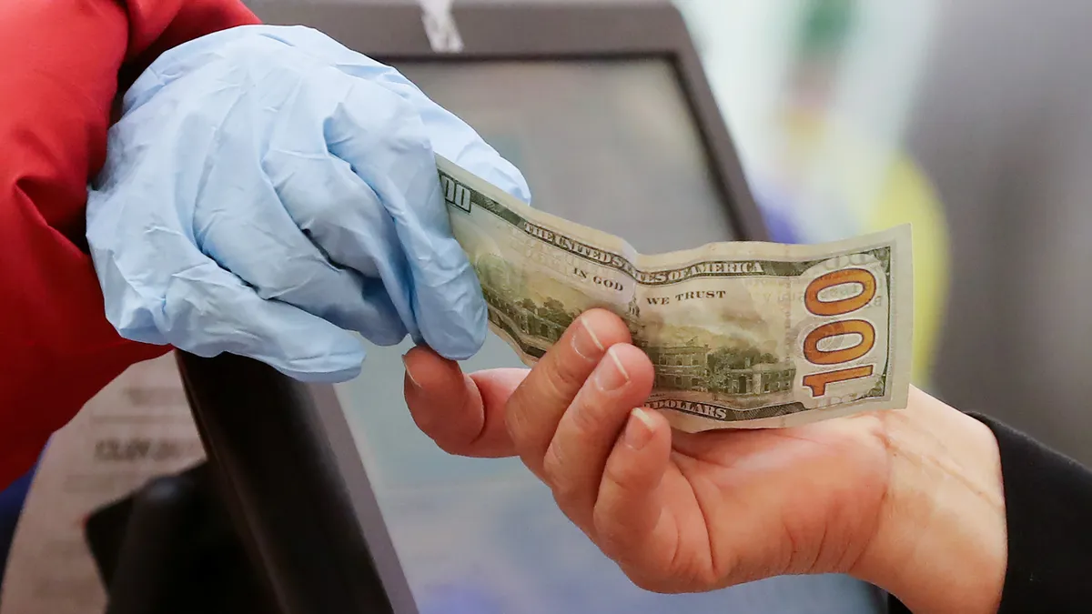 A plastic-gloved hand gives a $100 bill to another hand.