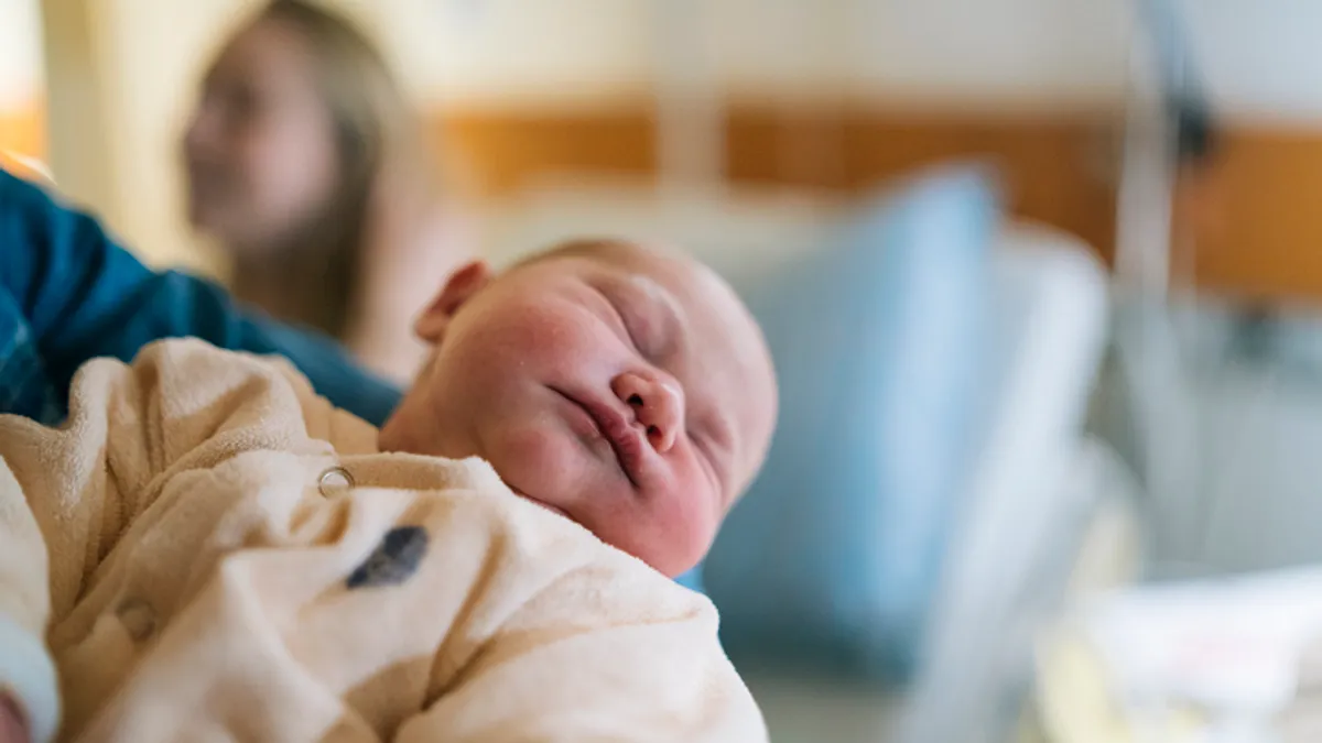 a father holds a baby in the hospital while the mother looks on