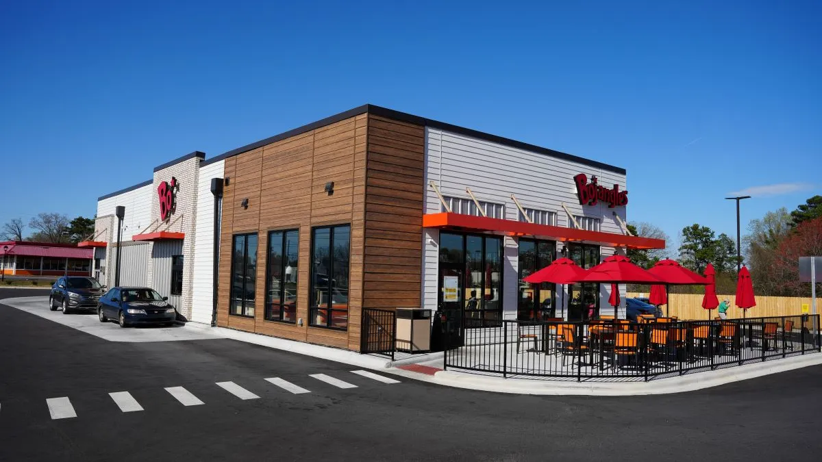 A building with white and brown siding with two black cars at a drive-thru. Signage says Bojangles