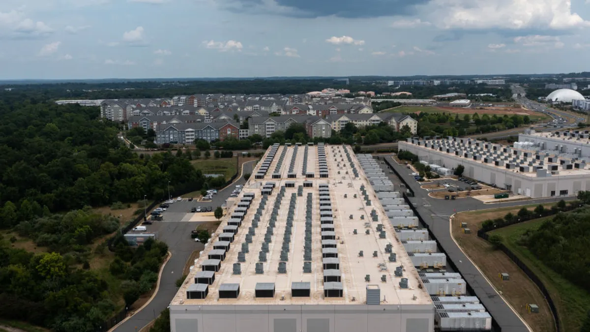 An aerial view of a large gray building amid trees that takes up most of the frame. It is level, and low to the ground.