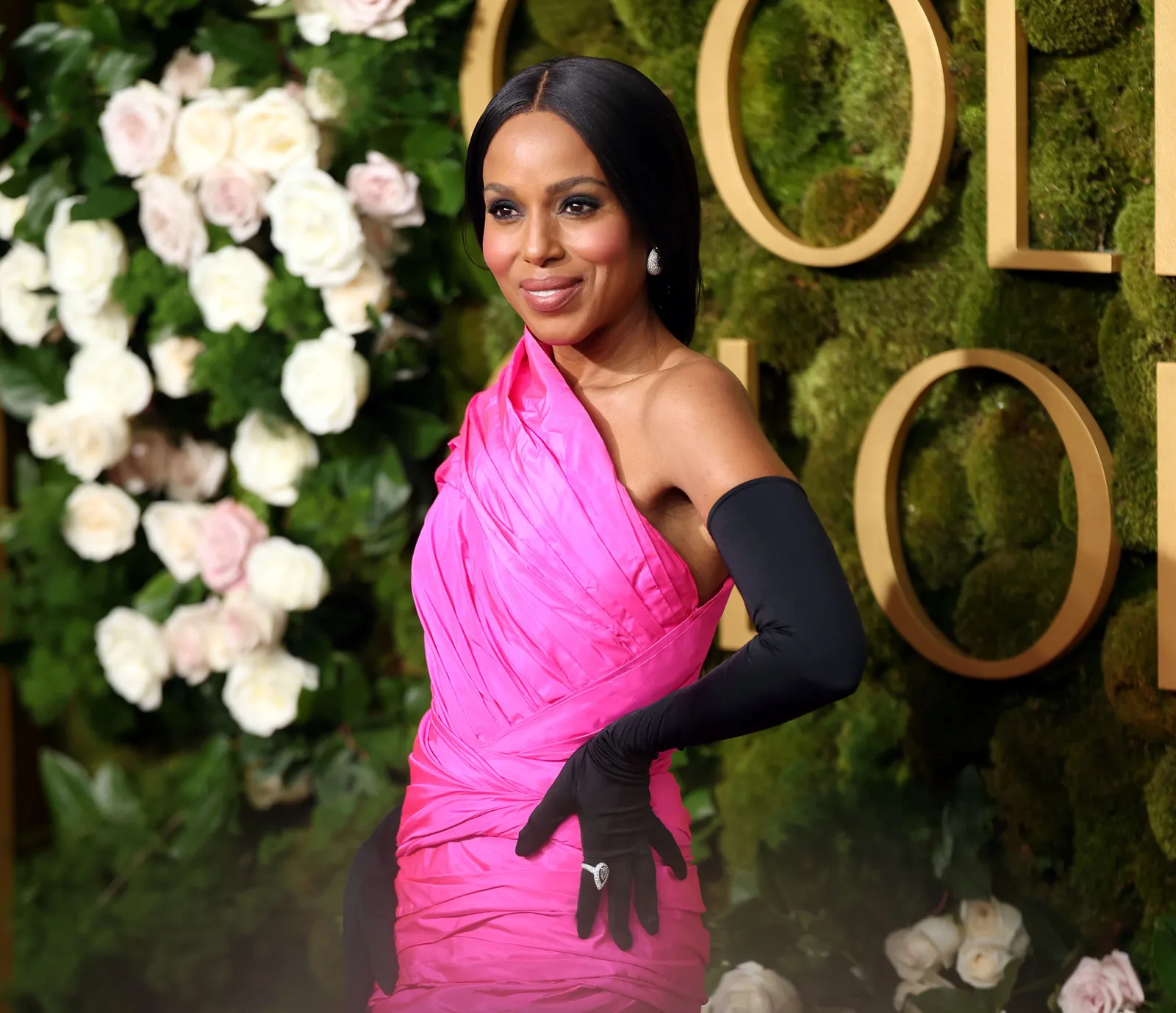 A person in a hot pink one shouldered gown and black opera gloves poses again a green background that reads Golden Globes.