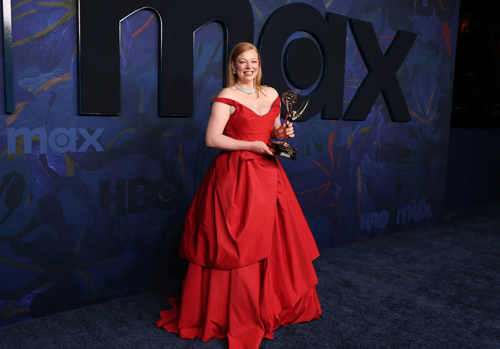 A person in a floor-length red gown holds an Emmy Award.