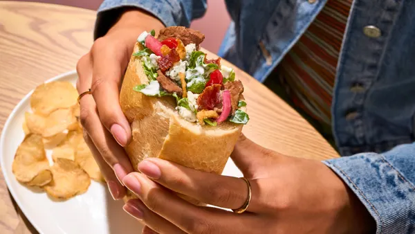 An image of a hand holding up a bread roll stuffed with a salad