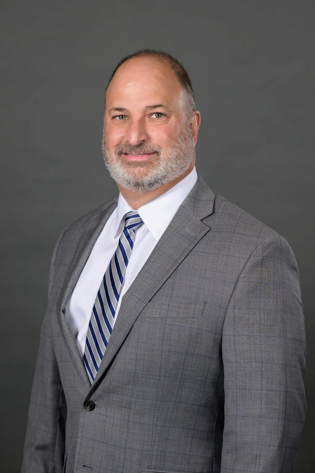 Portrait of a white man with gray beard wearing a gray suit against a gray backdrop