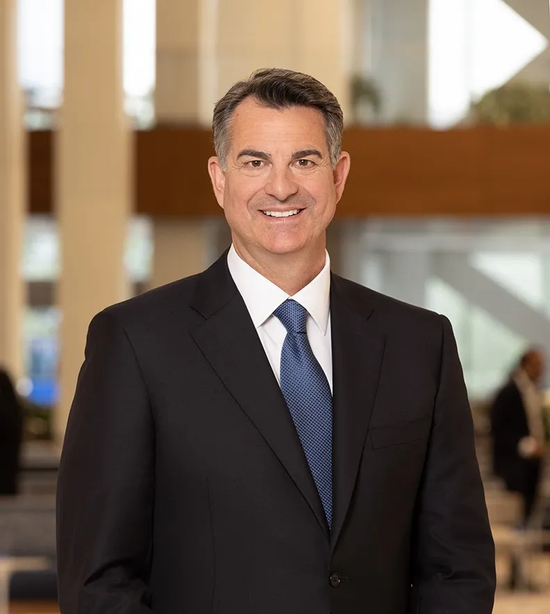 A person wearing a dark suit and blue tie smiles for the camera.