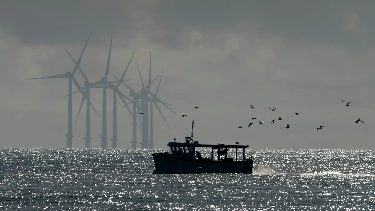 A ship is seen on a sparkling ocean with offshore wind turbines in the background.