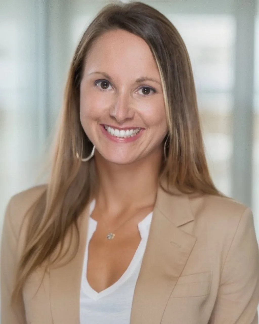 A woman with long hair wearing a beige blazer and white shirt