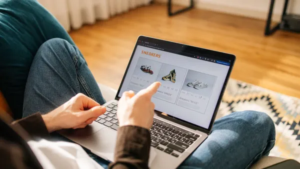A close-up shot of an unrecognizable man browsing for sneakers on his laptop while sitting on his couch.