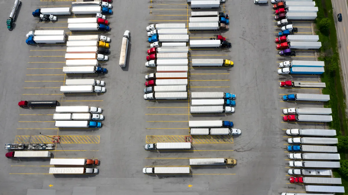 Aerial view of a large group of semi-trucks parked at a highway truck stop with scores of tractor-trailers present.