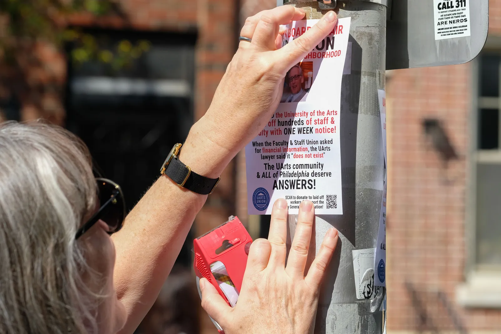 A person affixes a flyer on a public poll that reads, “The UArts community &amp; ALL of Philadelphia deserve ANSWERS!”